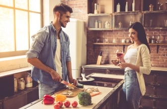 Man preparing dinner while woman watches on smiling