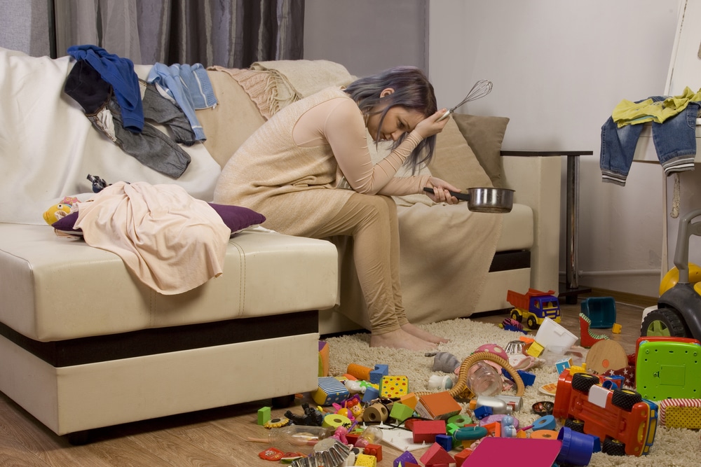 Fed up mother sat on sofa surrounded by clutter/mass