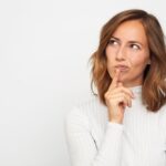 woman in white jumper thinking about investing in the ftse 100