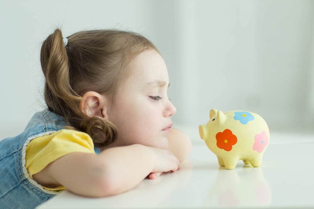 Little girl looking grumpily at piggy bank