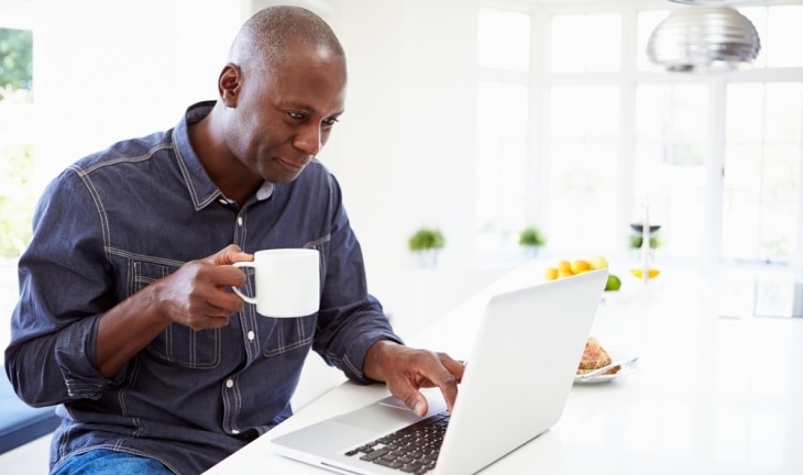 Middle aged man using Laptop and drinking from a mug