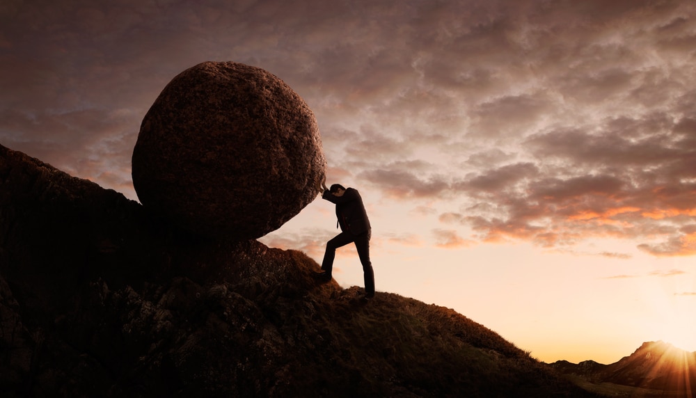 Effort concept - man pushing large boulder up a hill