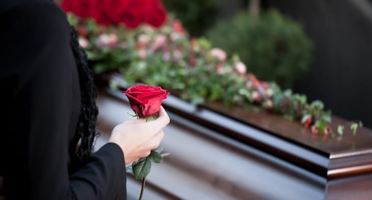Someone standing by a coffin holding a rose