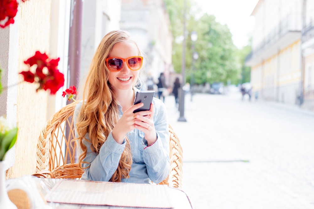Young Woman using smartphone outside a cafe in the sunshine