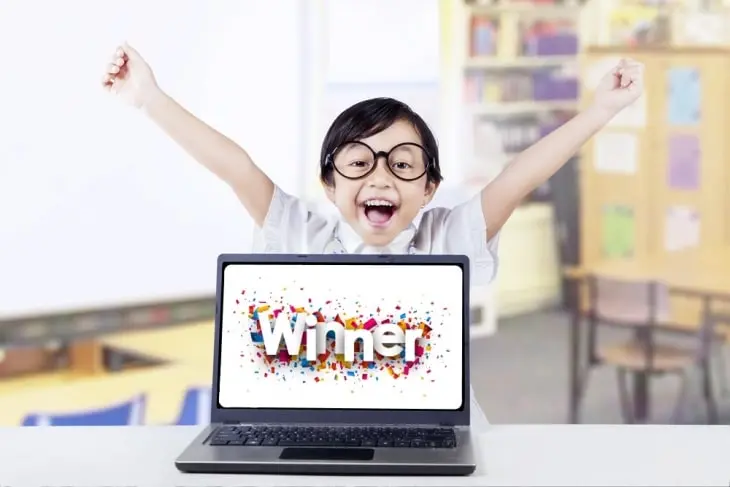 Cậu bé ăn mừng đằng sau chiếc máy tính xách tay có dòng chữ "Người chiến thắng" trên màn hình