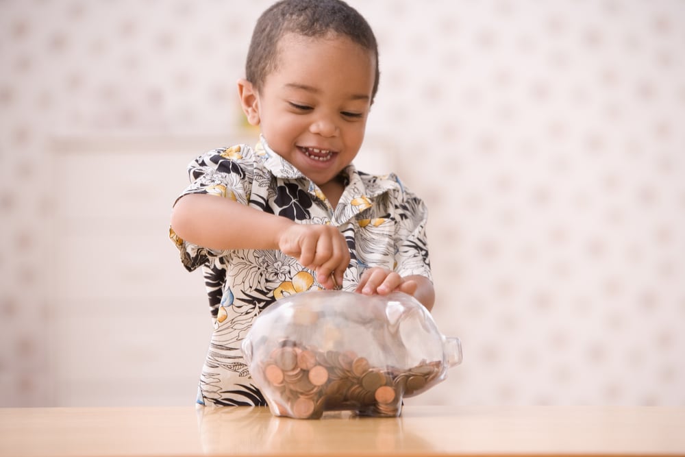 Little boy putting coins in glass piggy bank