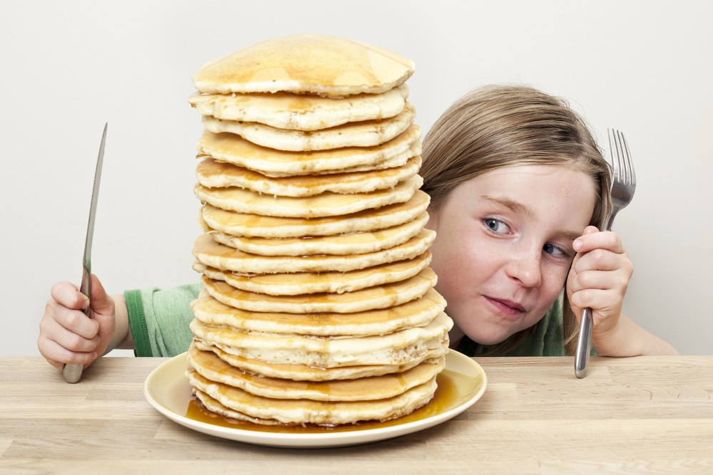 Little girl looking at big stack of pancakes