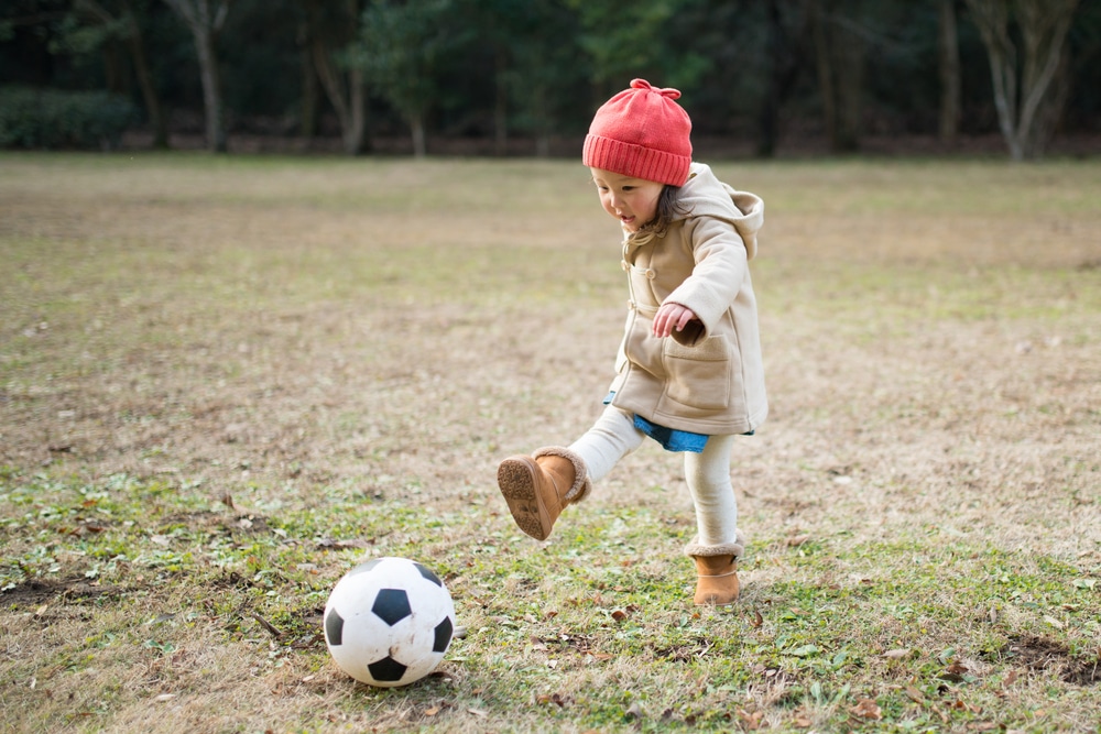 Little girl playing football on frosty grass