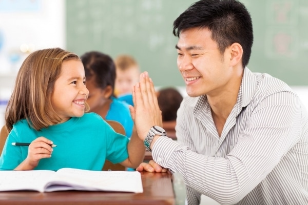 Male teacher high five-ing young student