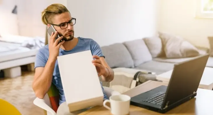 Confused man looking at a laptop screen while holding product box