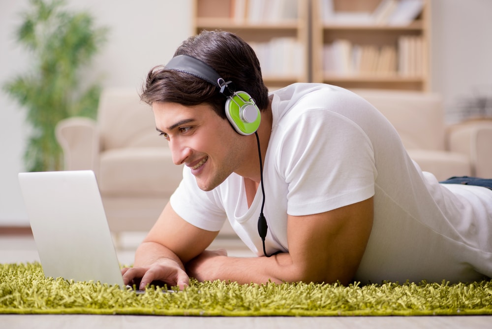 Young man lying on floor listening to music on laptop