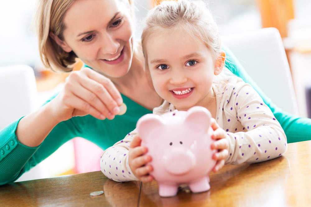 Mother and young daughter saving money in piggy bank