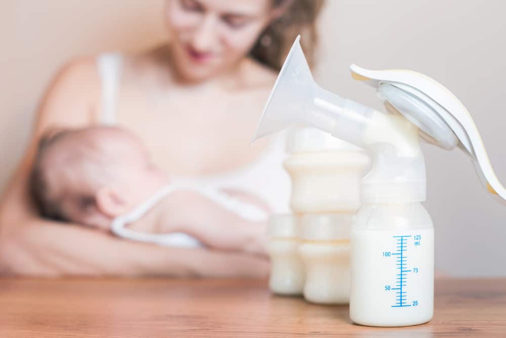 Breast pump and bottles with mother breast feeding in background