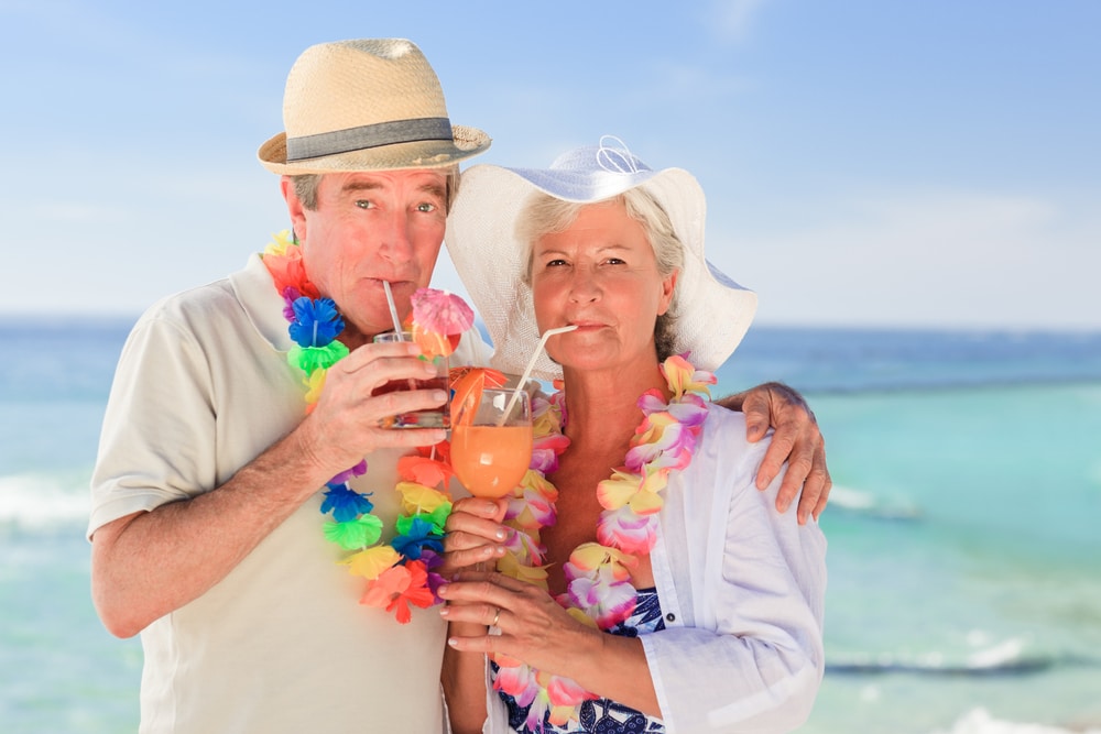 Elderly couple wearing leis and drinking cocktails on the beach