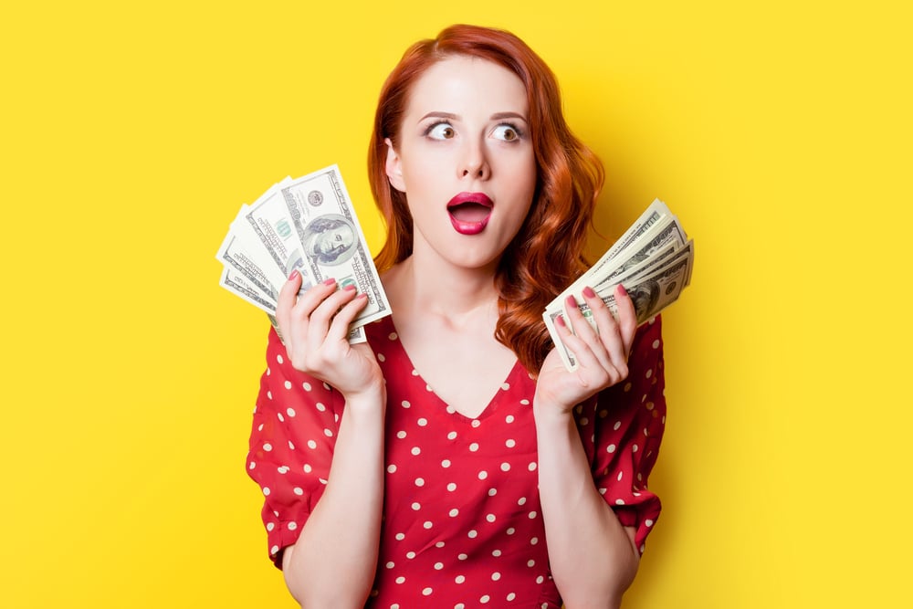 Shocked woman holding handfuls of dollars