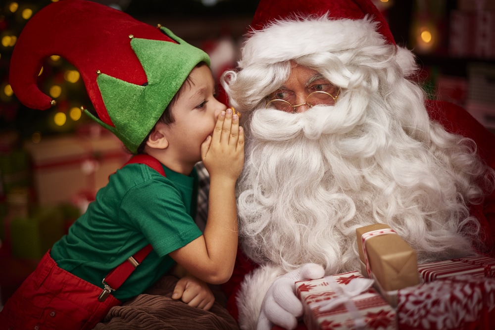 Little boy in elf costume whispering to santa