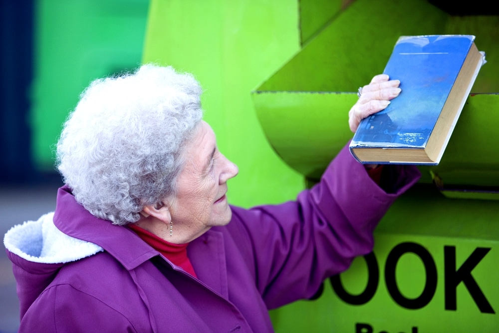 Elderly woman putting old book in recycling book-bank