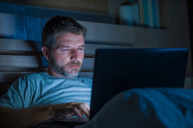 Sex addict watching porn on his laptop in bed.