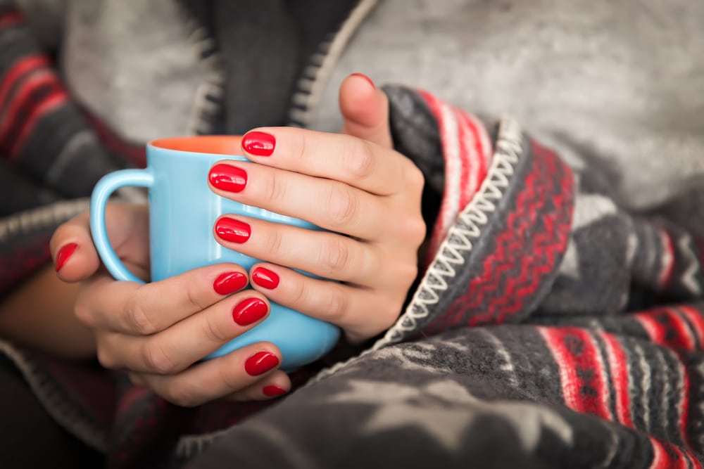 Woman holding mug of warm drink wrapped in blanket