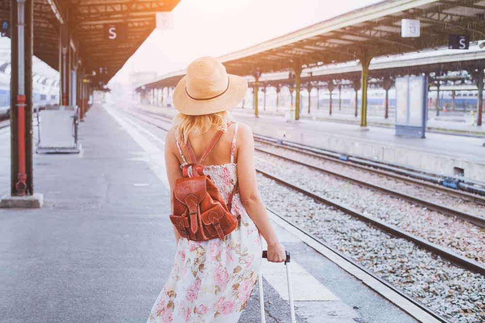 Woman in summer dress with suitcase at train station