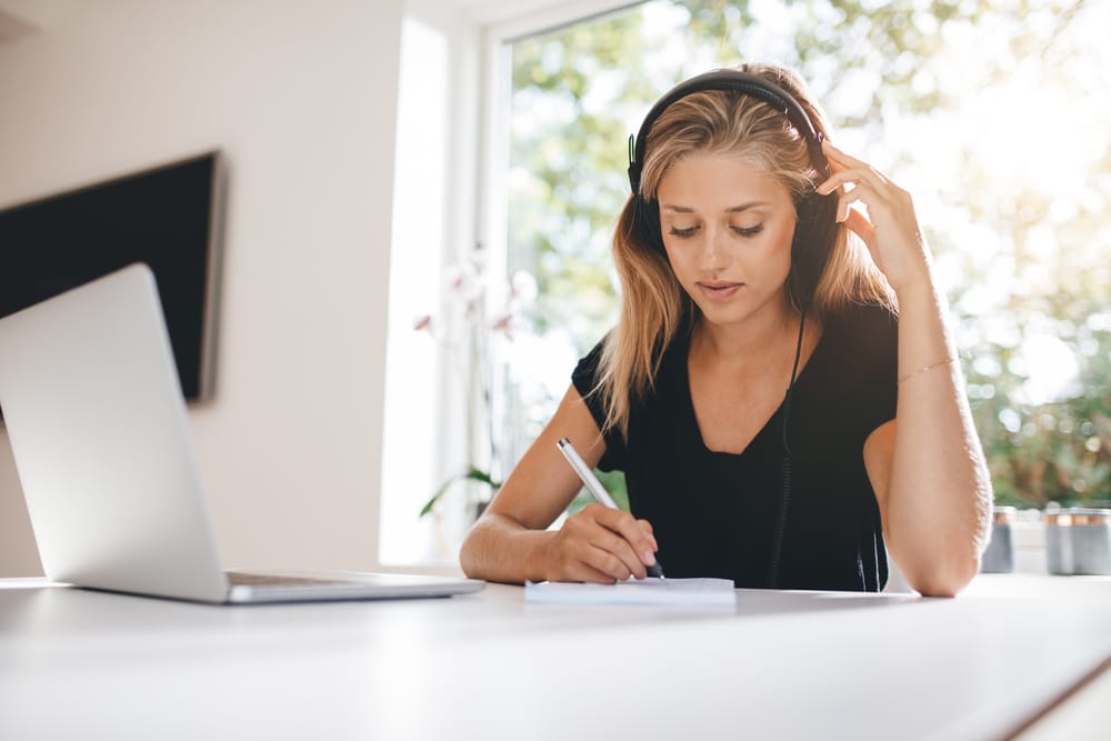 Woman listening to headphone and writing