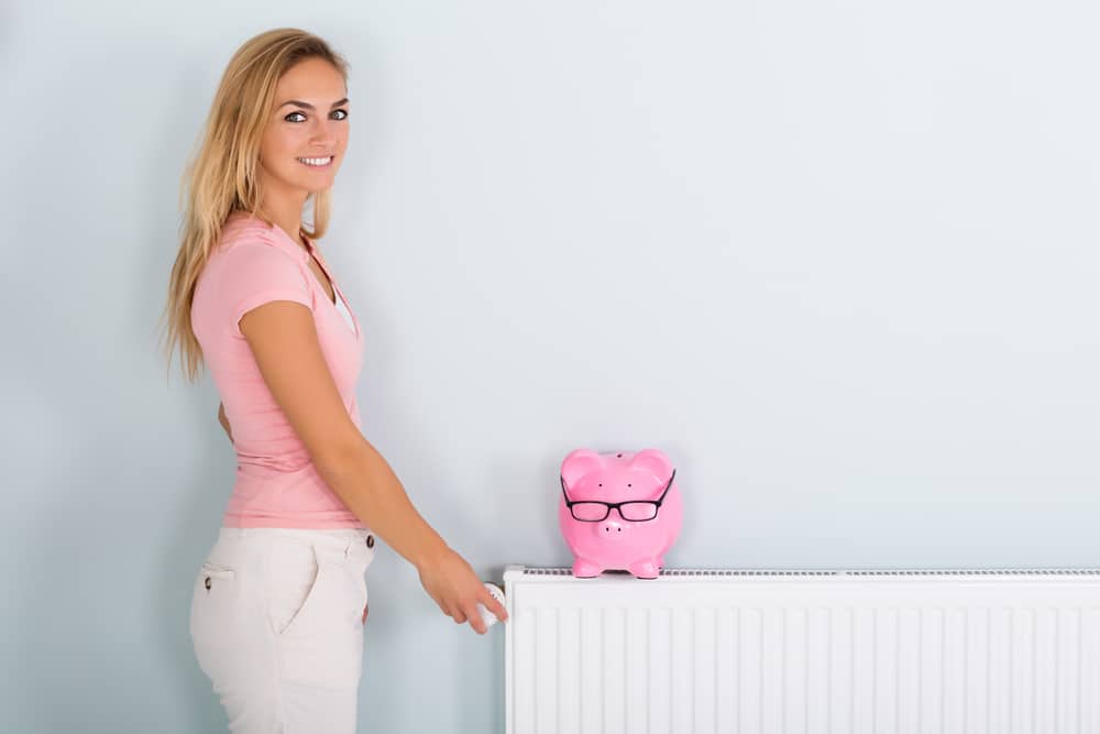 Woman next to radiator with piggy bank