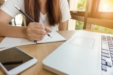 girl sat by laptop writing index list on piece of paper