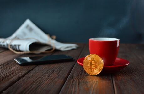 bitcoin leaning against coffee cup next to newspaper