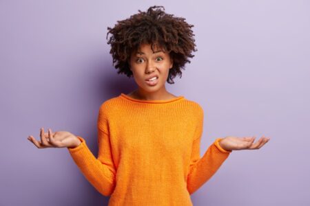 African American woman in orange jumper with hands out and confused face about a UK recession